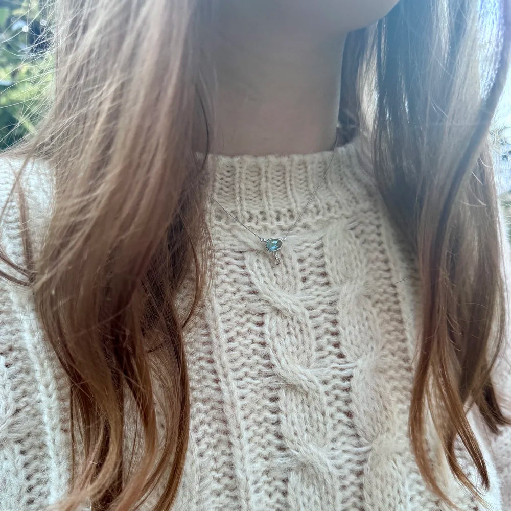 Collier argent et topaze bleue porté proche du cou, symbolisme céleste et spirituel.
