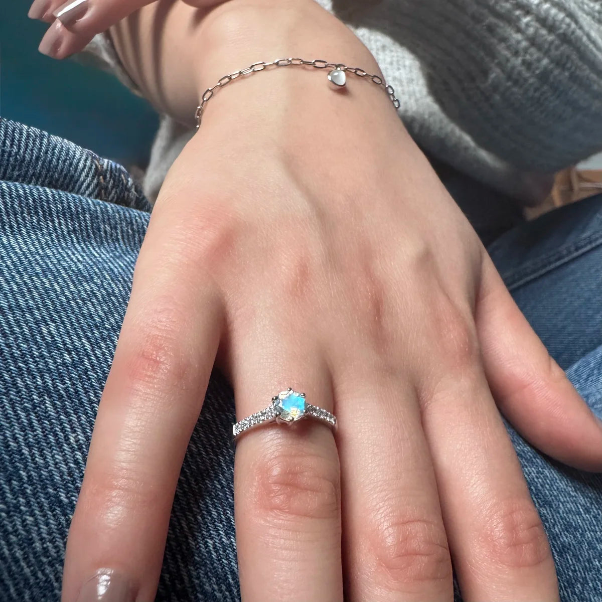 Main de femme portant une bague solitaire Pierre de Lune au reflet bleuté