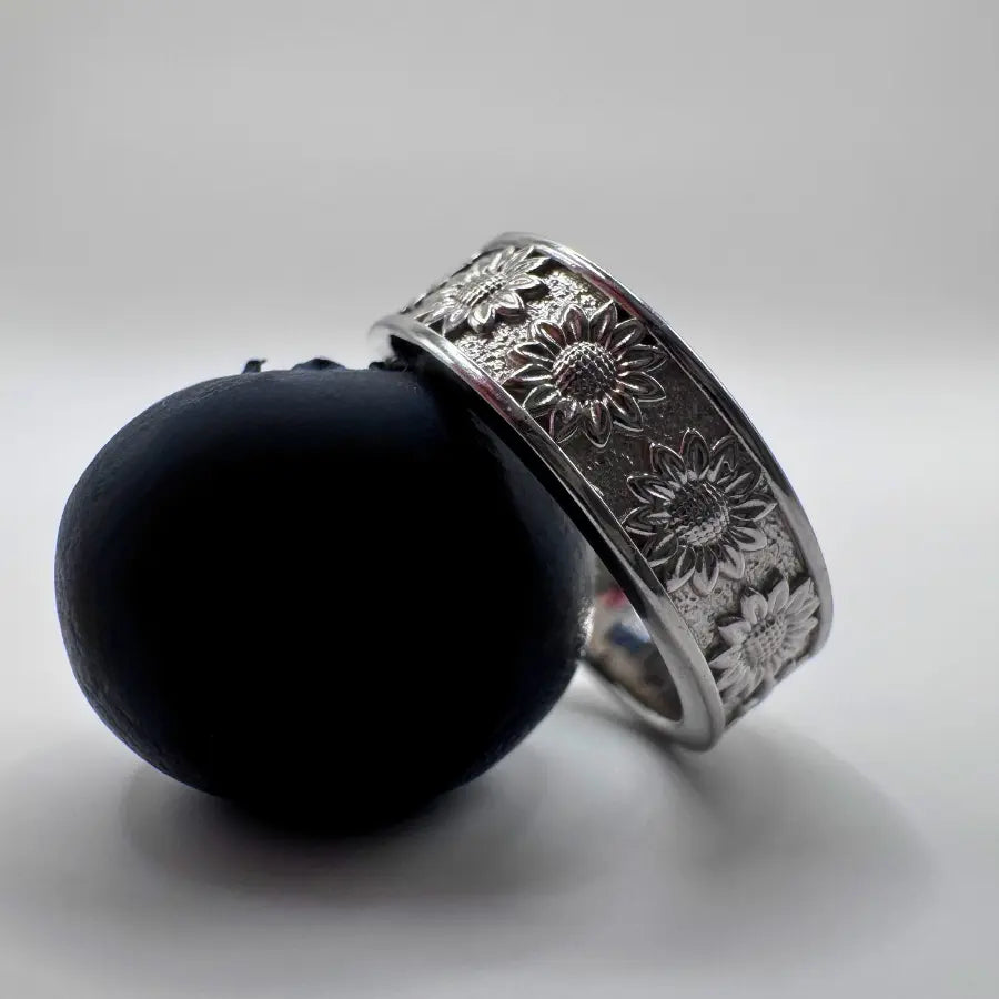 Bague argent motif végétal posée sur une myrtille, mettant en valeur la gravure florale des tournesols.