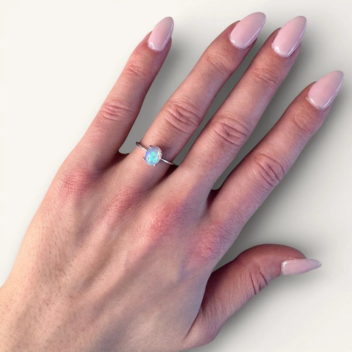 Bague fine en argent sertie d'une opale cabochon portée à l'annulaire. Rendu élégant et lumineux sur la main.