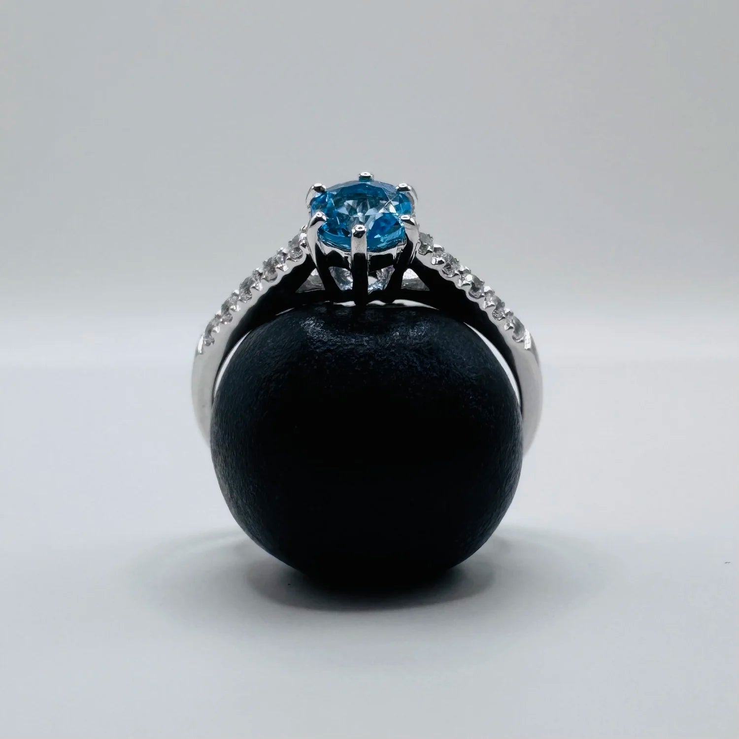 Bague solitaire Topaze bleue posée sur une myrtille et capturant la lumière du jour, bijou vibrant et céleste.