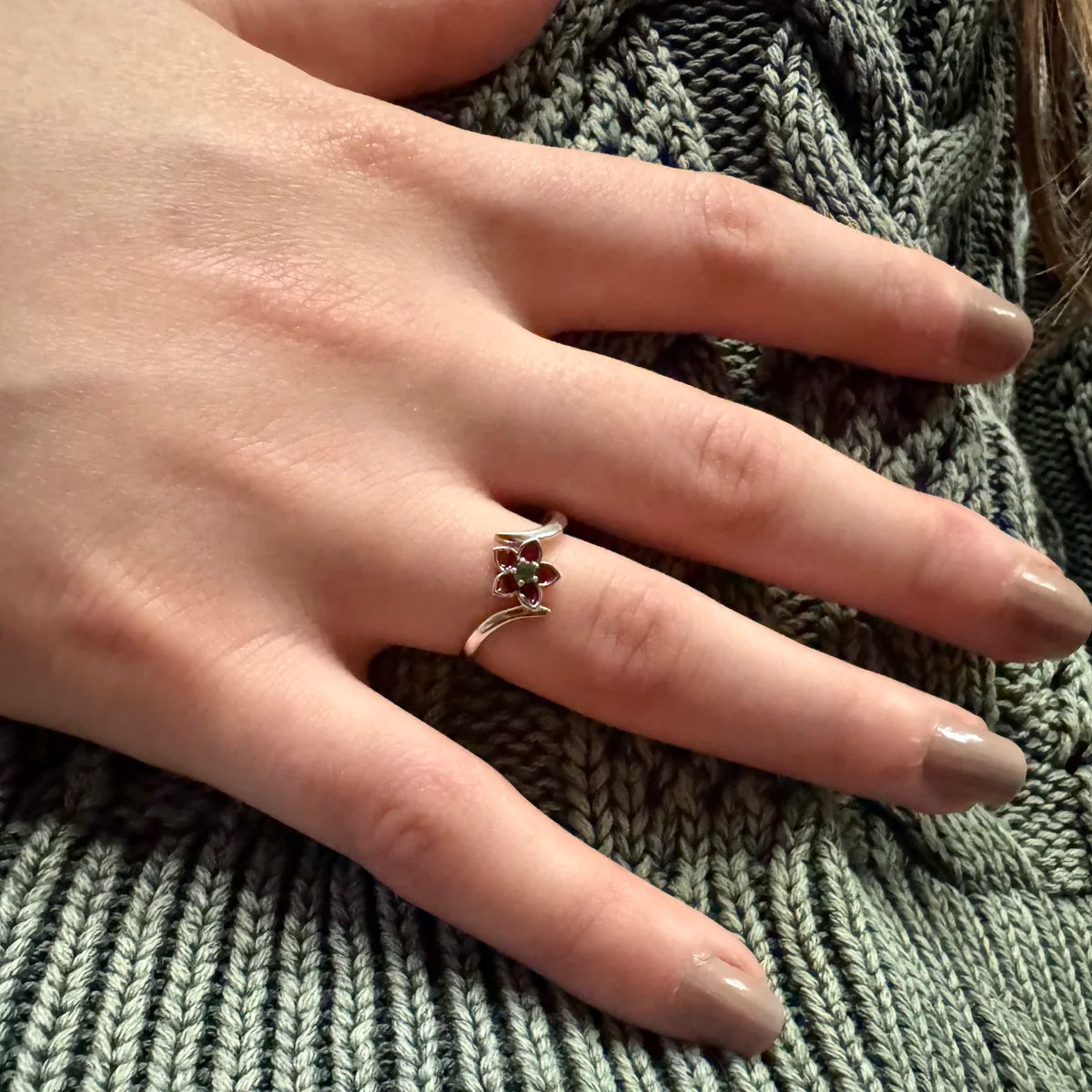 Bague fleur argent aux pétales rouges portée, main de femme sur un pull en maille verte.