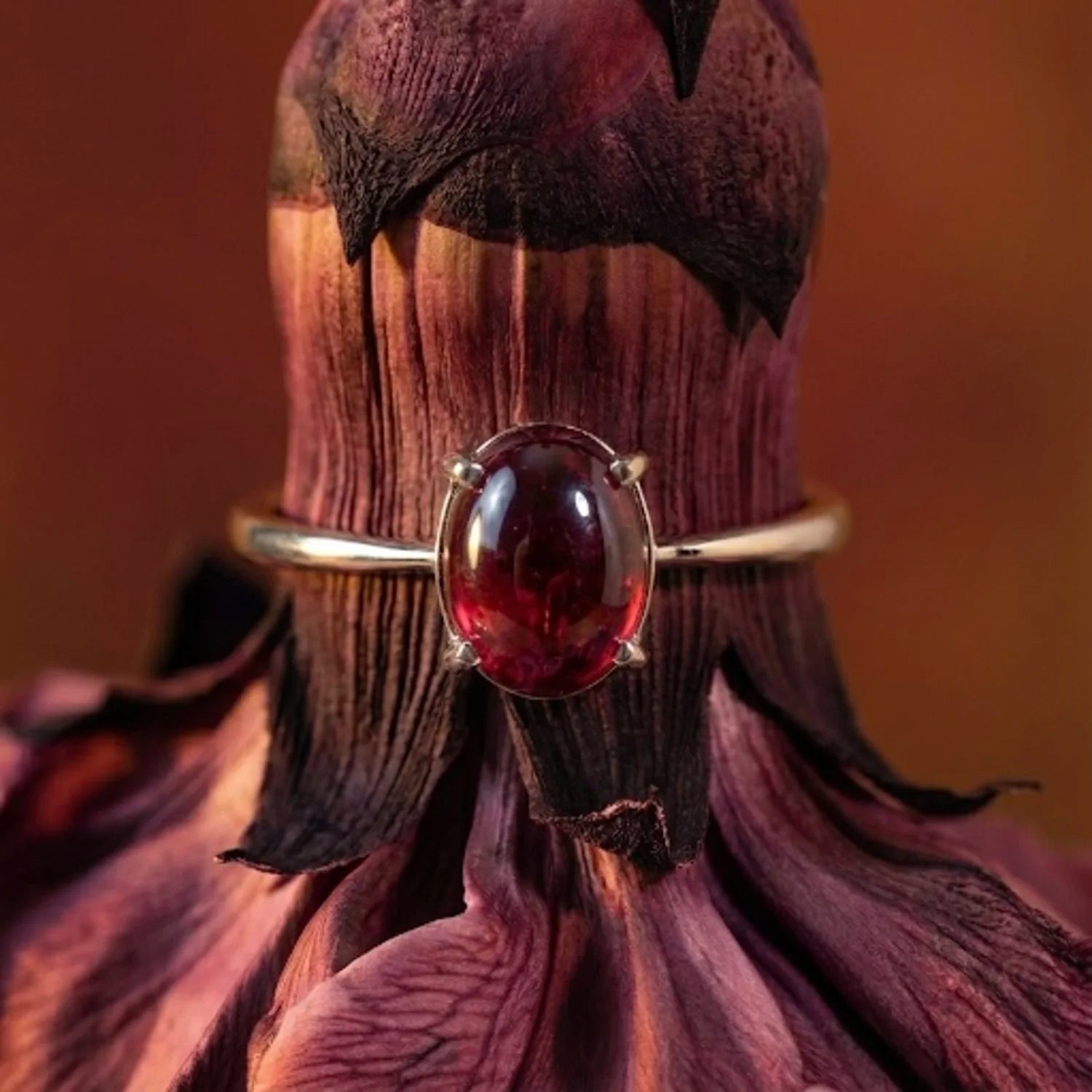 Gros plan sur le grenat rouge de la bague Aura, pierre lisse et sombre aux reflets de braise.