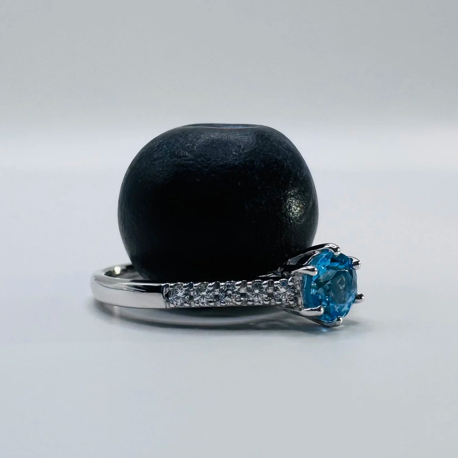 Architecture d'une bague solitaire argent, laissant passer la lumière à travers la Topaze bleue.