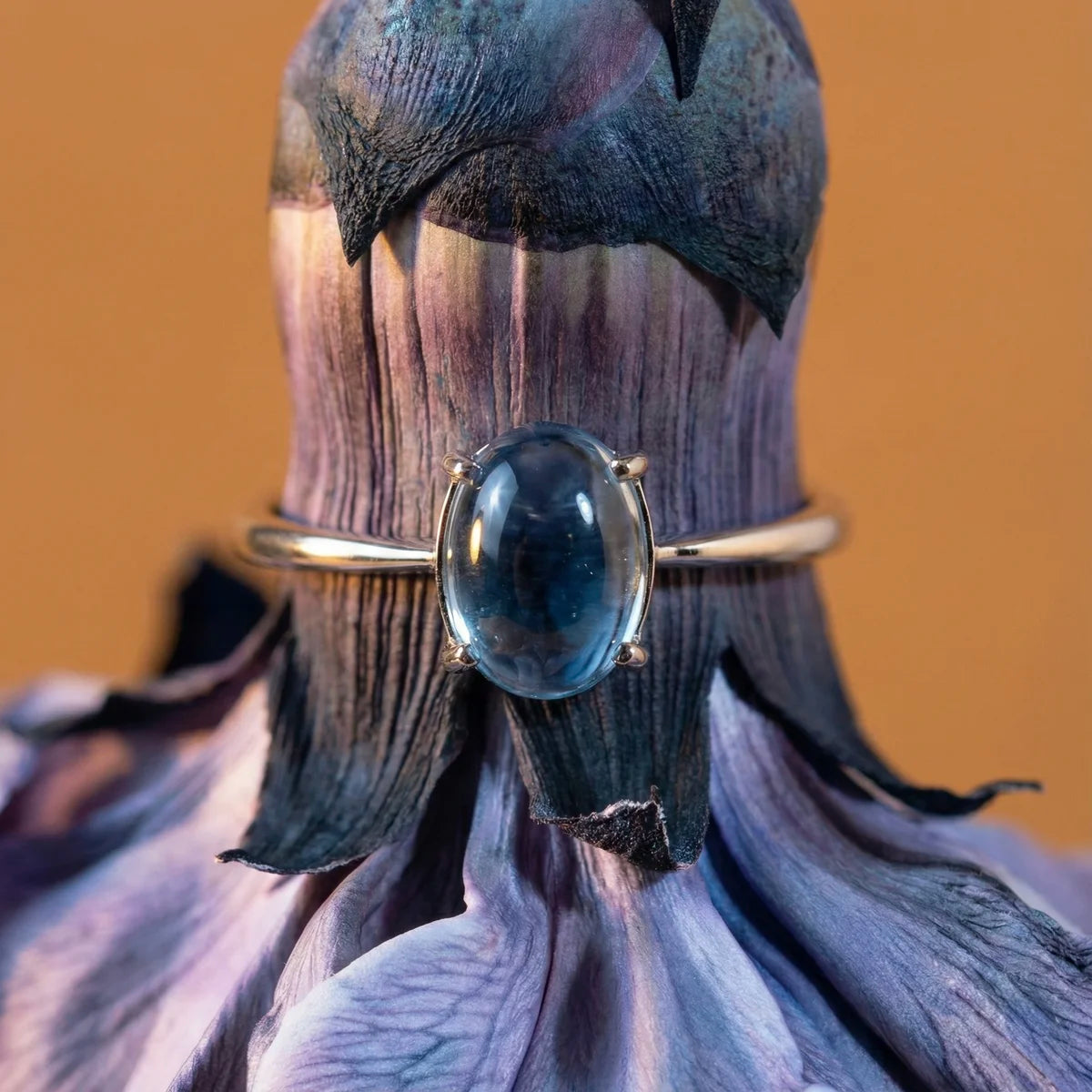 Gros plan sur la topaze bleue de la bague Aura présentée autour d'une fleur, pierre lisse et cristalline.