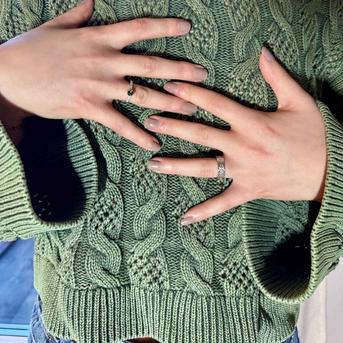 Bague solitaire Tourmaline verte portée sur une main posée sur un pull vert, bijou féerique et apaisant