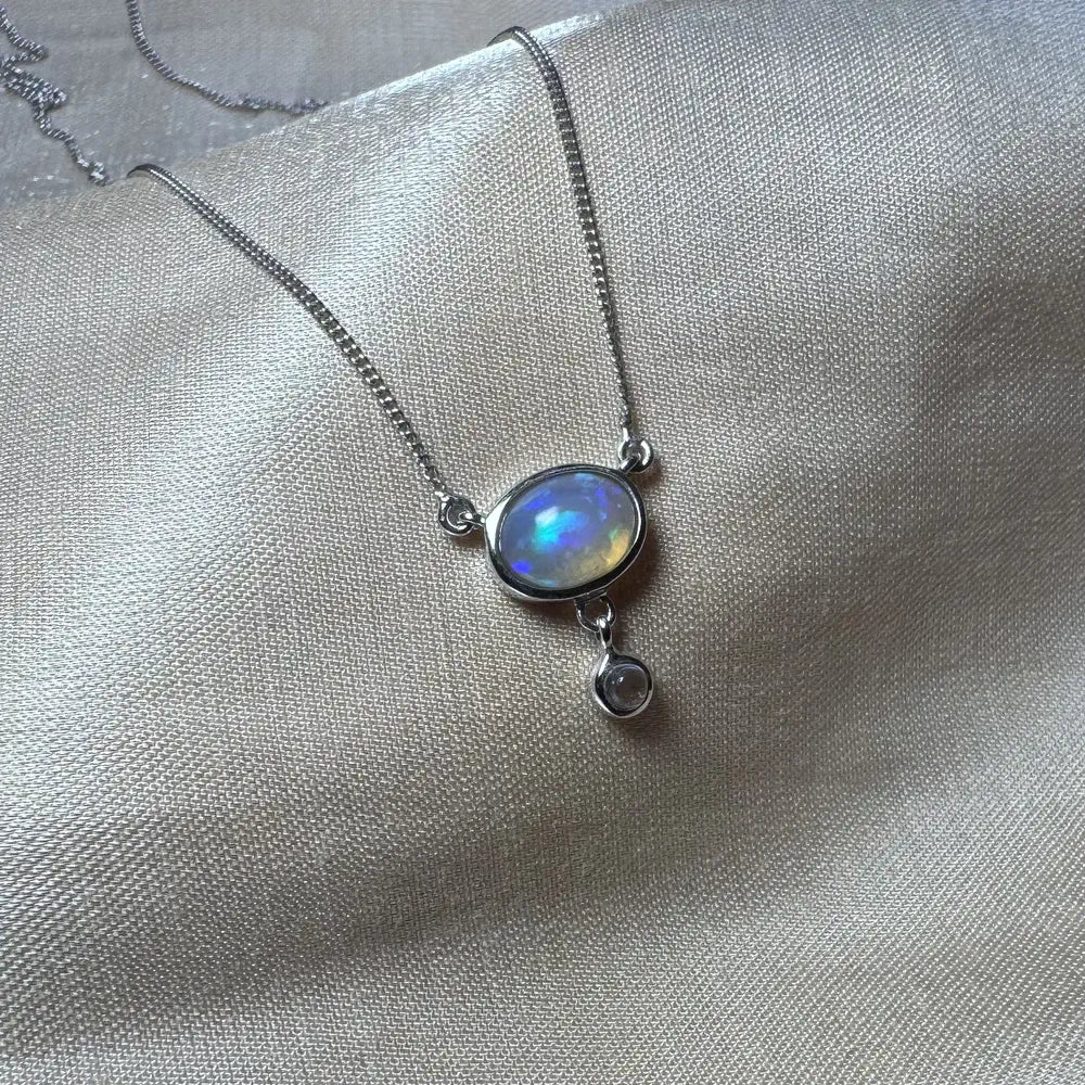 Collier argent et opale véritable posé sur un support en soie, symbolisme lunaire.