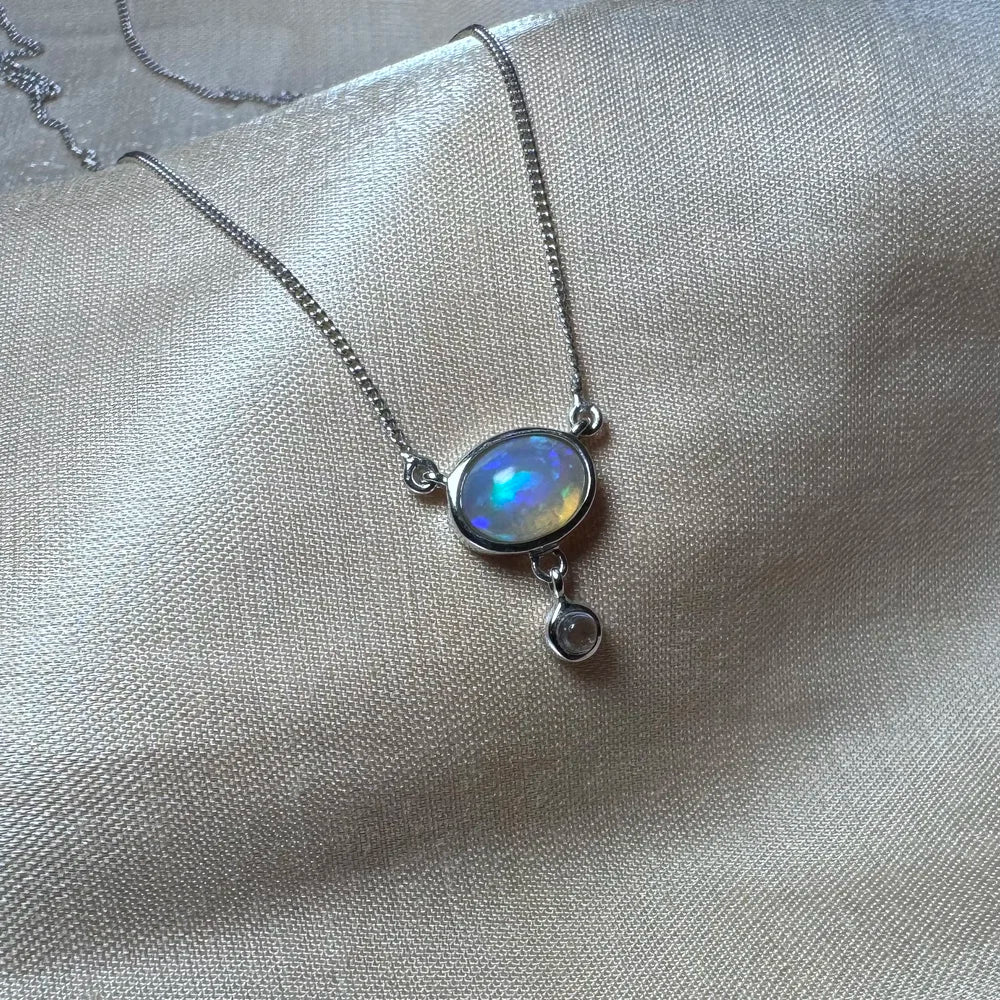 Collier argent et opale véritable posé sur un support en soie, symbolisme lunaire.