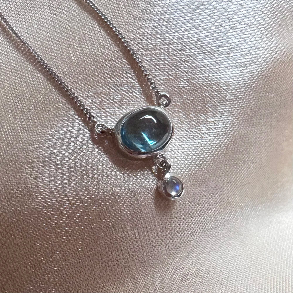 Zoom pendentif vertical topaze bleue et perle de lune, finitions artisanales en argent sterling 925.