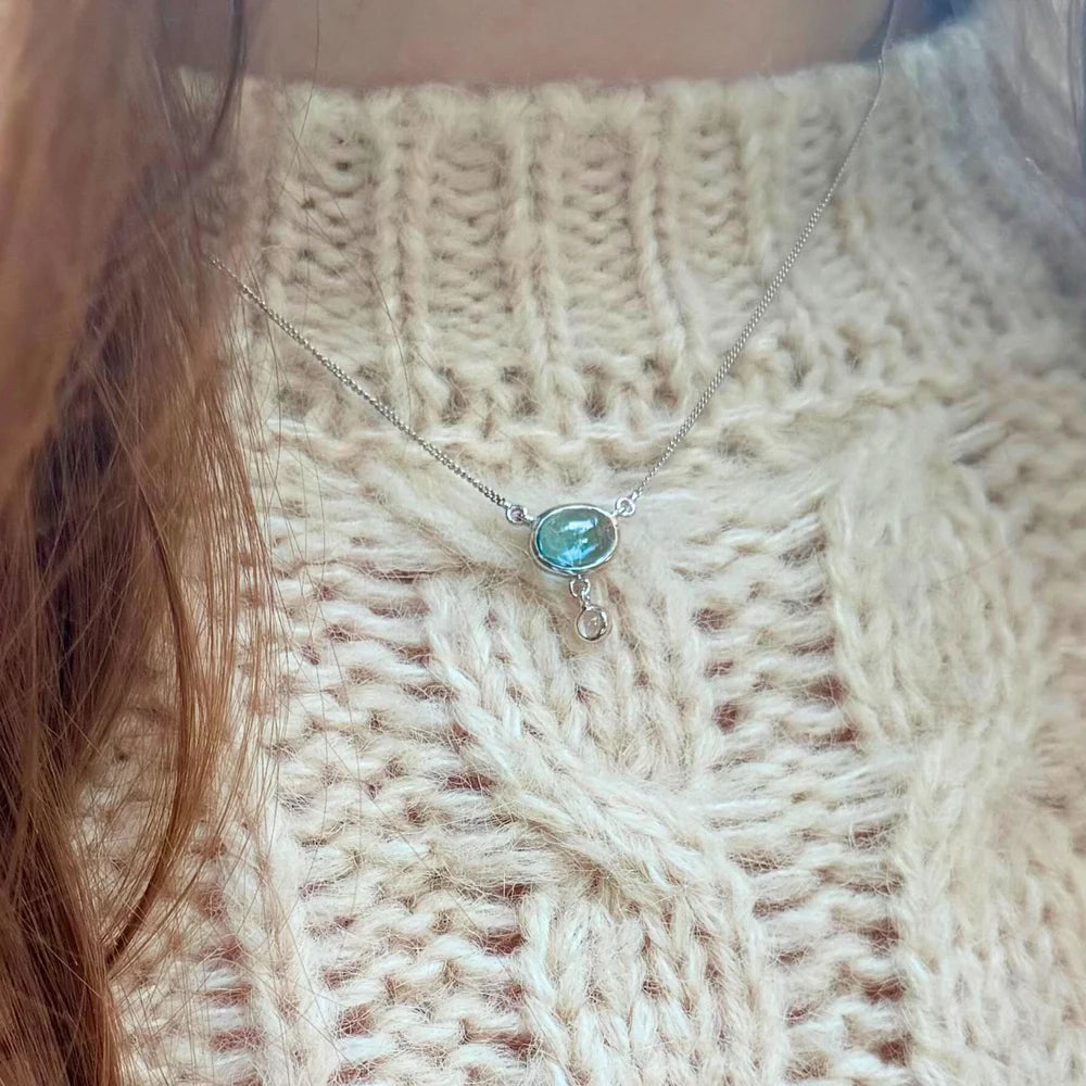 Détail du collier topaze bleue véritable Sillage Lunaire sur un pull en maille, style poétique et doux.